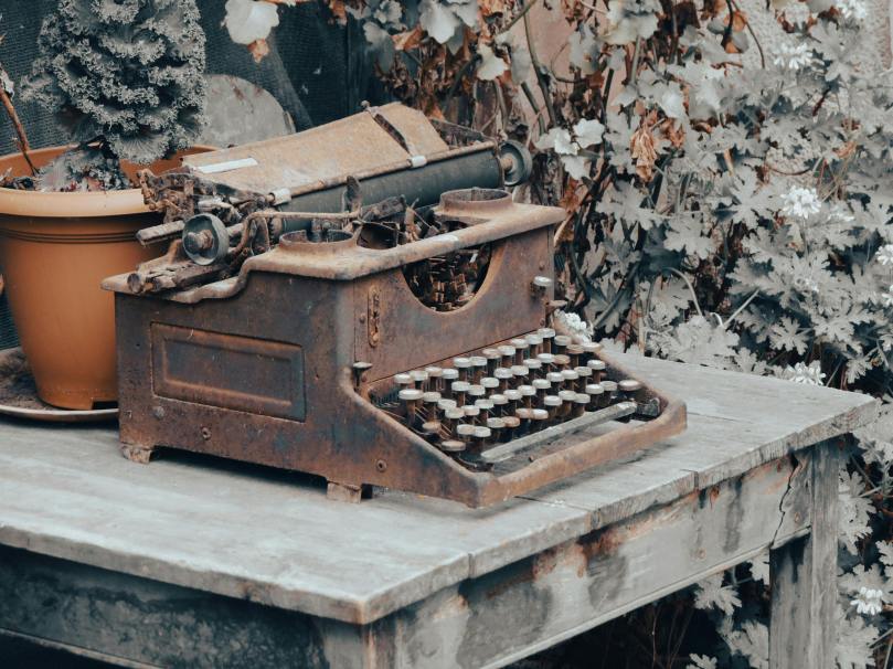 A dusty, rusted typewriter on a desk, also derelict.